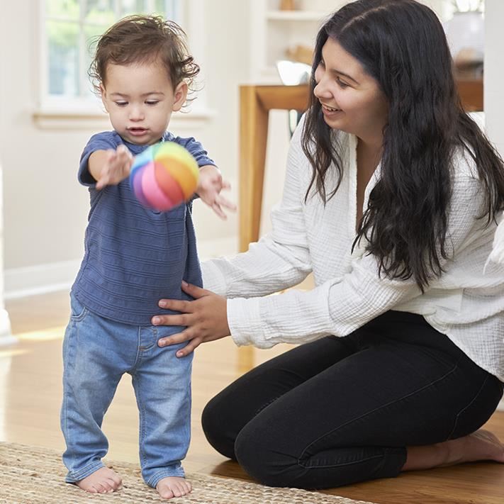 Young boy tossing ball with adult helping